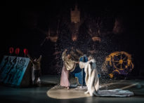 Dwóch aktorów na ciemnym tle tańczących na środku sceny w blasku reflektora, z góry pada na nich sztucznych śnieg. Z boku aktora w geście zwycięstwa. Na zdjęciu od lewej Elżbieta Węgrzyn, Kornelia Trawkowska oraz Wiesław Zanowicz.