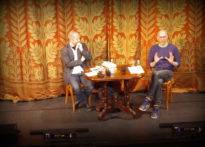 DWÓCH MĘŻCZYZN PRZY STOLIKU NA TLE OPUSZCZONEJ KURTYNY NA DUŻEJ SCENIE TEATRU POLSKIEGO W POZNANIU. OD LEWEJ PROFESOR PRZEMYSŁAW CZAPLIŃSKI I JAN SOWA. ZDJĘCIE ILUSTRACYJNE DO CYKLU NIE-BOSKIE NARRACJE. O LĘKU I GNIEWIE ROZMOWY Z PISARZAMI