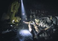 Na pierwszym planie aktor leżący na ziemi w samej bieliźnie a nad nim pochylająca sie kobieta, na drugim planie aktorzy oraz publiczność