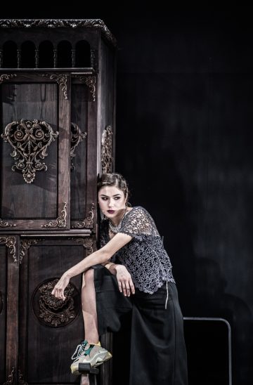 Aktorka stojąca na scenie przy dużej szafie z noga wspartą o element szafy