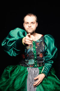 Portret mężczyzny ubranego w damską suknie wskazującego coś palcem